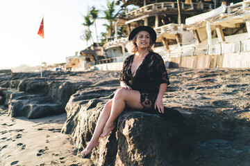 Young woman in black swimsuit enjoying bikini season for tanning and sunbathing on tropical beach, attractive female dressed in swimwear recreating and dreaming on seashore at Seychelles island