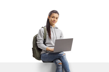 Female student with a backpack sitting on a blank panel with a laptop