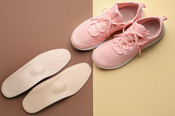 Pair of orthopedic insoles and shoes on color background