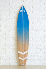 Modern surfboard near white brick wall in room