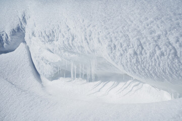 A snow drift of large size. Icicles melt in the sun. A white inflatable looms over the river.