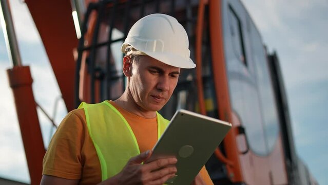 worker in hard a hat with digital tablet near excavator. construction site driver business with online digital tablet. industry construction concept. worker hard hat near excavator truck in uniform.