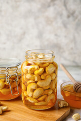 Board with jars of sweet cashew nuts in honey on grunge background