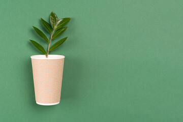 Kraft paper coffee cup with green leaves - biodegradable, compostable paper utensils for hot drinks. Paper cup on green background with copy space. Environmental conservation concept. Selective focus