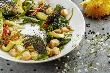 Avocado salad with baby spinach and pomegranate on a black plate on a slate,stone or concrete background.Top view with copy space