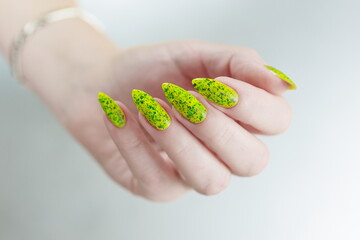 Female hand with long nails and a bottle of bright yellow green neon nail polish