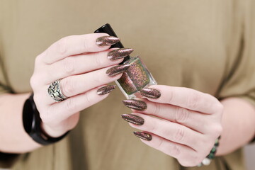 Female hand with long nails and a bottle of brown green nail polish