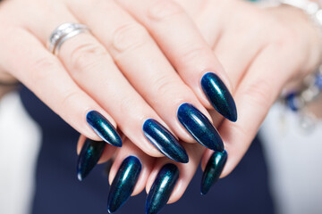 Woman's beautiful hand with long nails and turquoise green and blue manicure with bottles of nail...