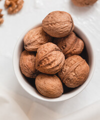 Whole brown walnuts close up in a white bowl on a white background. Healthy eating concept.