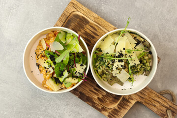 Risotto with tomatoes, greens and parmesan in bowls on wood board on gray background. Restaurant dish delivery. Top view. Free space for text. Healthy food concept.