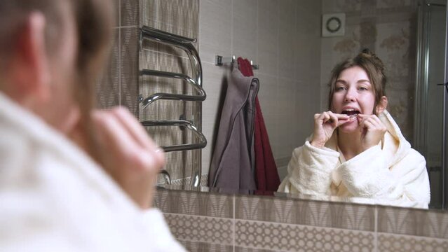 Front view through a mirror of a woman in the bathroom removing an invisible clear aligner from her lower jaw and showing a smile. Bite correction