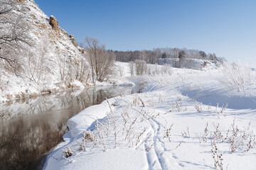 The river flows along the rock of the banks covered with snow. Winter landscape, cold season frosty weather, sunny day, blue sky.