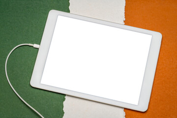 mockup of digital tablet with a blank isolated screen (clipping path included) against paper abstract in colors of Irish national flag, green, white and orange