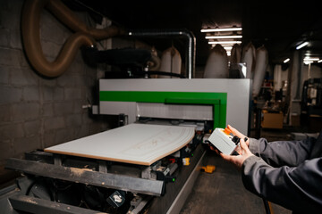 hands of the worker holding the control panel of the machine of processing of furniture accessories which is in the background