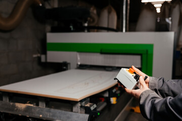 hands of the worker holding the control panel of the machine of processing of furniture accessories which is in the background