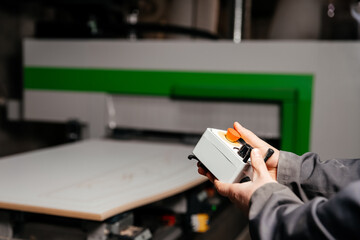 hands of the worker holding the control panel of the machine of processing of furniture accessories which is in the background
