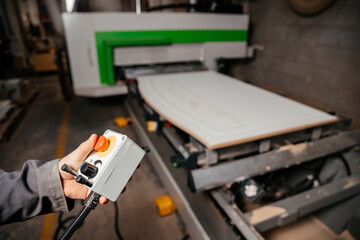 hands of the worker holding the control panel of the machine of processing of furniture accessories which is in the background