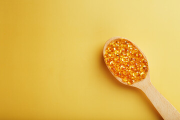 Fish oil capsules in a wooden spoon on a bright yellow background