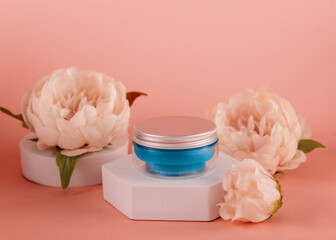 a blue  jar of cream on a white prop among peonies on a pink background