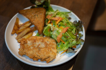 delicious homemade menu, Fried Sea Bass fish fillet in breadcrumbs, buttered bread and fresh vegetable salad served with French Fries on an old wooden table 