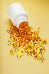 Golden Omega-3 fish oil capsules poured out of a jar on a yellow background