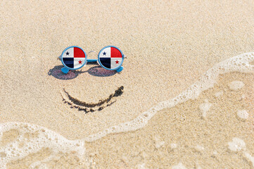 Fototapeta na wymiar A painted smile on the sand and sunglasses with the flag of the Panama. The concept of a positive and successful holiday in the resort of the Panama.
