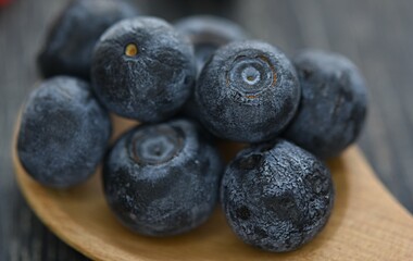 blue blueberries on a wooden spoon close-up on a dark wooden background