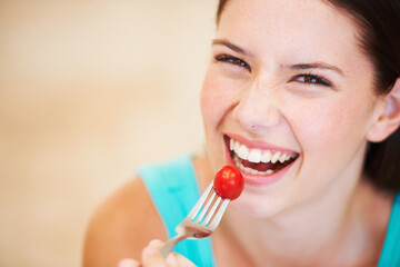 Enjoying a baby tomato. Portrait of a beautiful young woman eating a baby tomato.