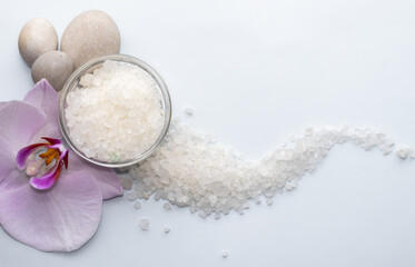 purple orchid flower on light blue background and sea salt. spa and skincare concept. relax, meditation mood. natural. mineral grains, wellnes.space for text. sea salt arranged wave shape.