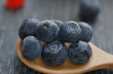blue blueberries on a wooden spoon close-up on a dark wooden background