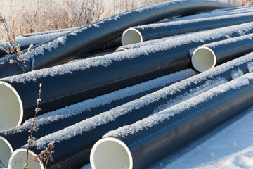 Plastic water pipes. Black PVC tubes plastic pipes stacked on white snow background. Heating houses in winter.