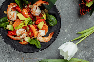 Shrimps salad with cherry tomatoes, cucumeber, avocado, lettuce and pomegranate on dish. Healthy seafood concept. Tasty grilled prawn shrimp and mix vegetable salad on black, top view
