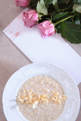 Obraz na płótnie Canvas Oatmeal porridge with almonds. Breakfast in the cafe. Postcard and pink roses on a light background. An empty space for the inscription on the postcard.Top view.Flat lay.