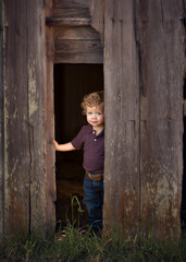 Young child peeking out from an old barn on the western ranch