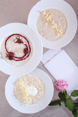 Porridge in an assortment in white dishes. Healthy food. Breakfast in cafe.Photos for menu.Postcard and pink roses on light background.An empty space for inscription on postcard.Top view.Flat lay.