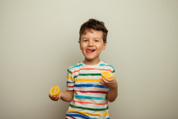 little boy eating lemon, sour taste, makes grimace, facial emotions negative, in white striped T-shirt, isolated white background, copy space. - obrazy, fototapety, plakaty