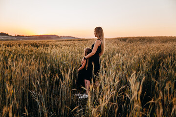 Rear view of mother and her daughter staying in golden wheat field on sunset