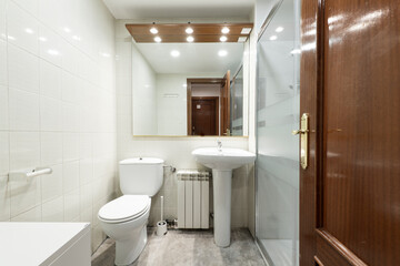 Fototapeta na wymiar Toilet with gray concrete floor, glass partitioned shower stall, white porcelain sink below square mirror with wooden door