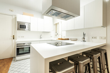 Beautiful modern kitchen with an island and metal stools, one-piece countertop, plain white cabinets without handles and stainless steel appliances