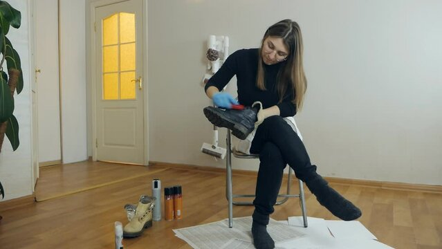 A beautiful young woman brushes her shoes before going to work. Shoe care at home