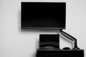 A modern computer monitor is mounted on a gas lift bracket next to a laptop and a computer mouse....