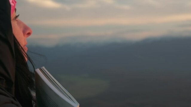 a girl looks at the sunset, holding a book in her hands against the background of mountains