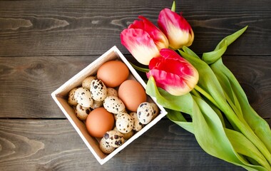 Decorative Easter card.  On a wooden brown background lies a white wooden box with Easter eggs, early spring flowers tulips.  Flat lay, close-up.  Easter bright holiday concept.