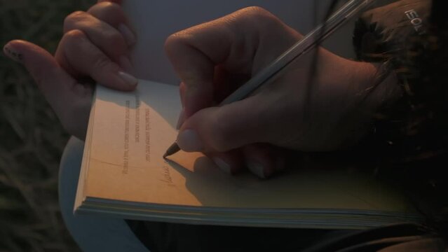 a girl is sitting on a mountain at sunset writing something in a notebook