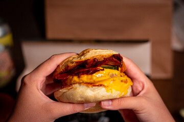 Woman's hands holding delicious hamburger with meat, yellow cheese and bacon. Smash Burger with cheese sauce, pickles and bacon