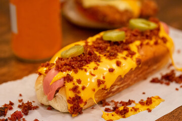 Hot dog with sauerkraut, bacon, pickles and cheese - close-up on the table