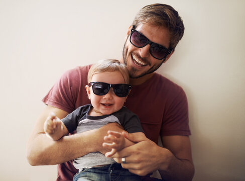 Coolness runs in this family. A young father and his infant son wearing matching sunglasses and laughing.