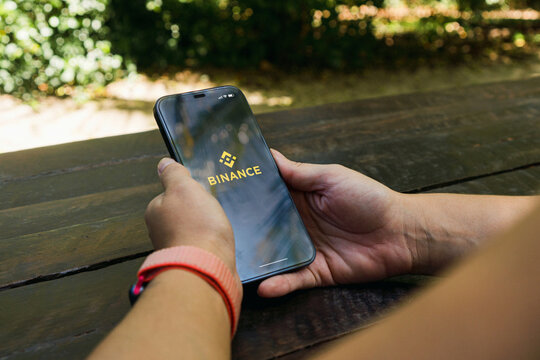 Girl in the park holding a smartphone with Binance cryptocurrency exchange app on the screen. Rustic wooden table. Rio de Janeiro, RJ, Brazil. March 2022