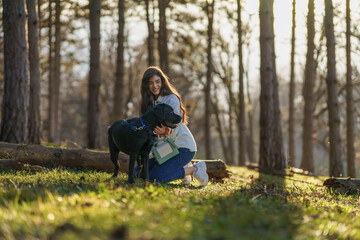 A smiling young attractive woman playing and walking with her Labrador puppy in a city park. The concept of pet and animal care.