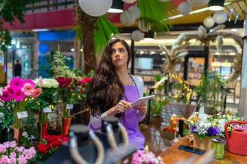 A beautiful worried and tired florist is sitting at the counter thinking about work, looking at her notebook